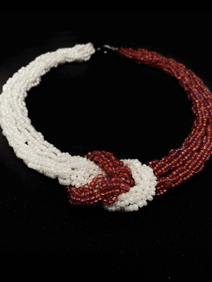 A multi-strand beaded necklace featuring white and red beads, with a central knot.