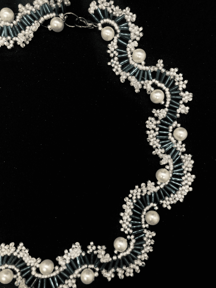 A handcrafted beaded necklace with a combination of white and teal beads, and pearl accents.