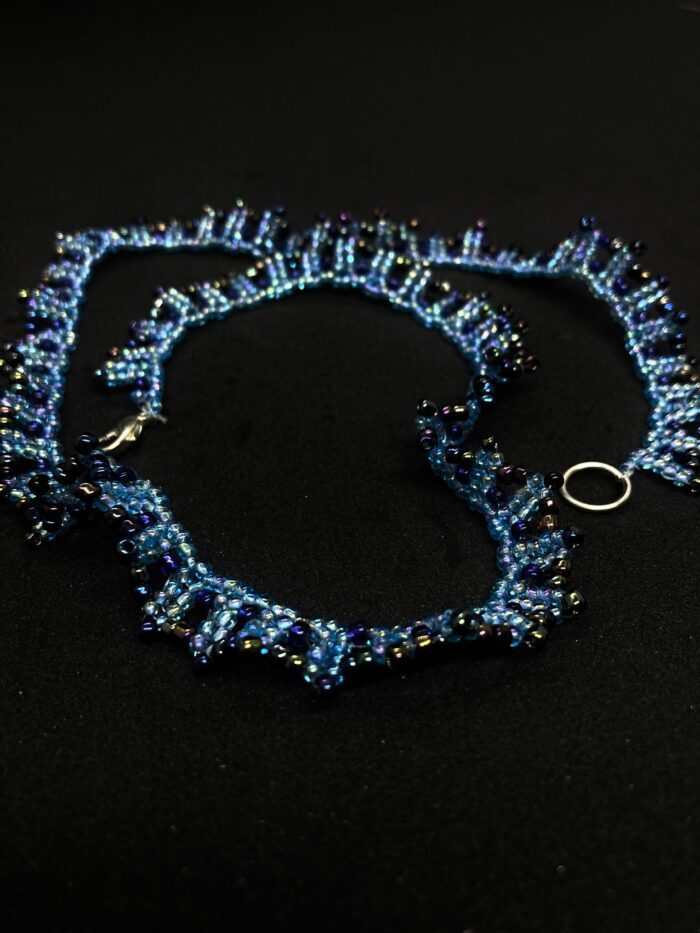 A handcrafted beaded necklace with a flowing design and a mix of blue and purple hues.