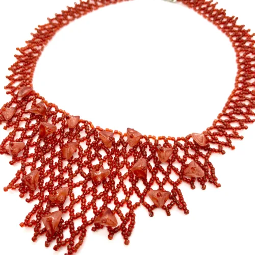 Close-up of a handmade red seed bead necklace with triangular glass accents, laid flat on a white background.